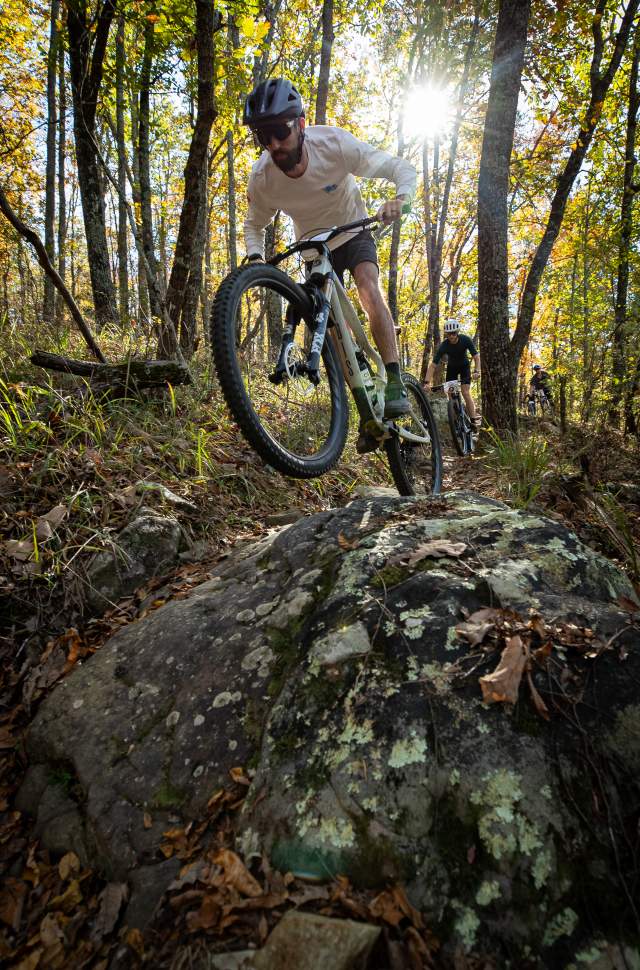 A biker rides over a large boulder on the trail at Oak Mountain State Park.