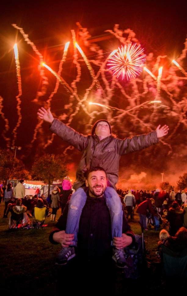 A father with child on shoulders with Fireworks display in sky