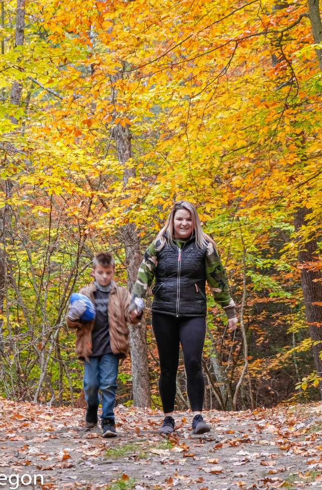 Mother and son walk holding hands along autumn colored trail in Muskegon State Park. The little boy holds a football.