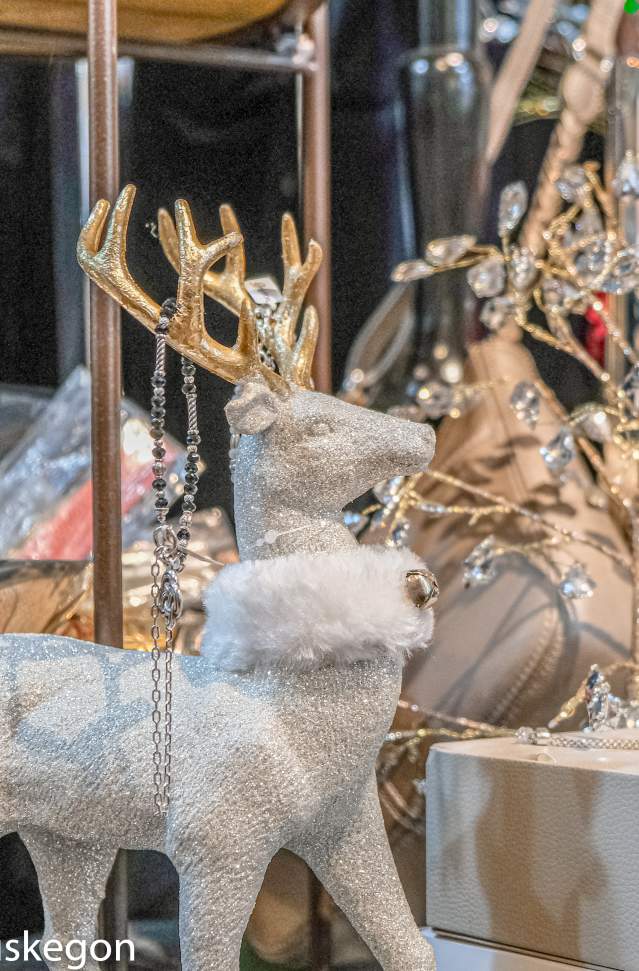 store holiday display of of white and sparkly deer with fur collar and gold antlers stands before display of shiny bracelets and leather purse and box