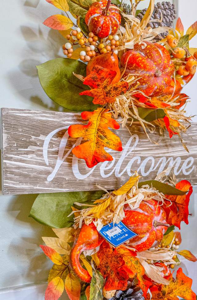 autumn decor of orange leave and foliage with wooden sign that says welcome hangs on wall