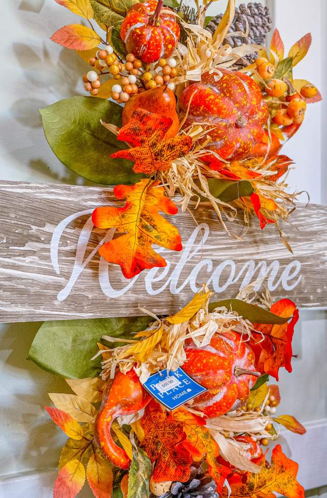 autumn decor of orange leave and foliage with wooden sign that says welcome hangs on wall
