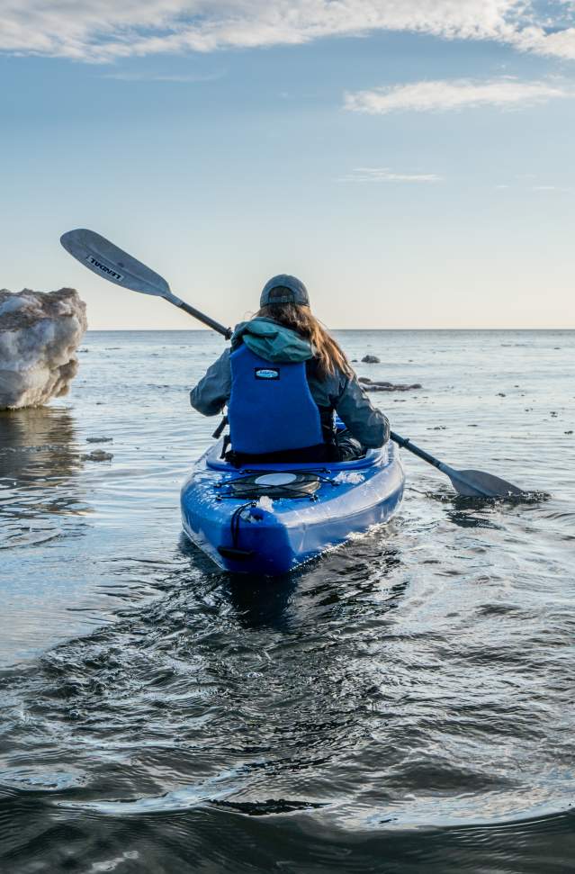 woman kayaks away from photographer between ice formations on Lake Michigan