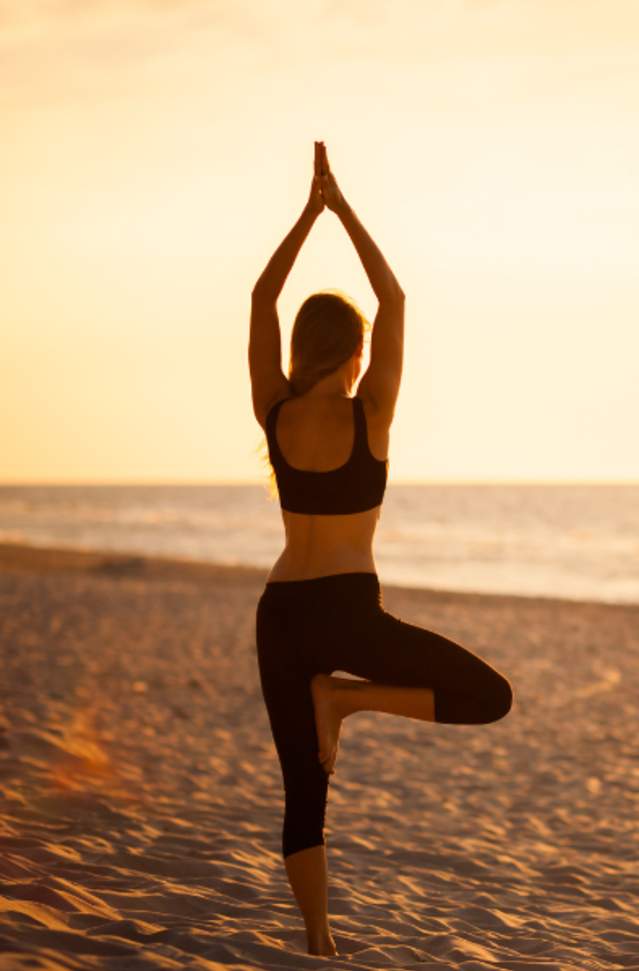 woman in yoga pose on beach at sunset