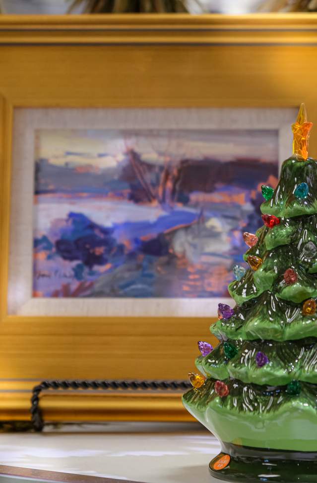 A decorative ceramic Christmas tree with colorful lights on display, flanked by a framed landscape painting and a small bird ornament on the left.