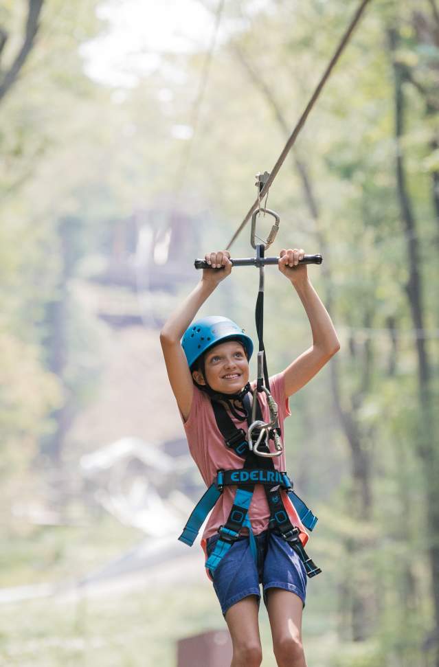 young smiling girl on zipline sails through muskegon state park forest