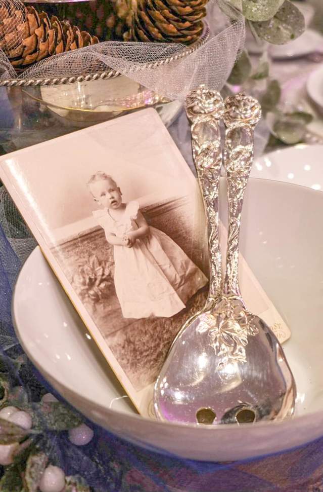 vintage photo of toddler sits in vintage white bowl with old silver spoons on holiday decorated table