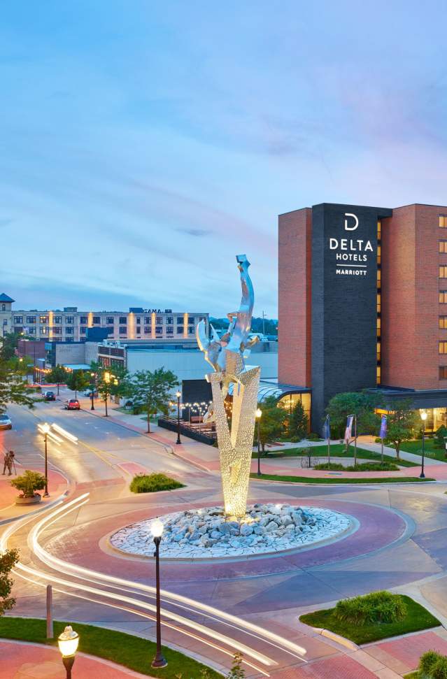 View of the Delta Hotels building and Frauenthal theater at twilight with a circular road and central statue in the foreground.