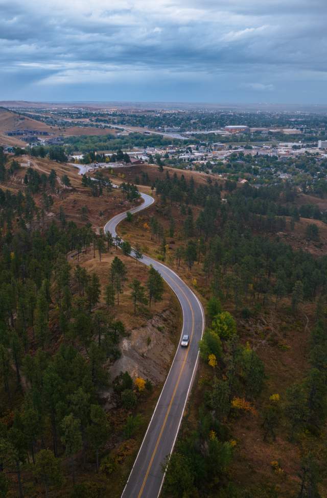 drone shot of car weaaving along skyline drive in rapid city, sd with city in background