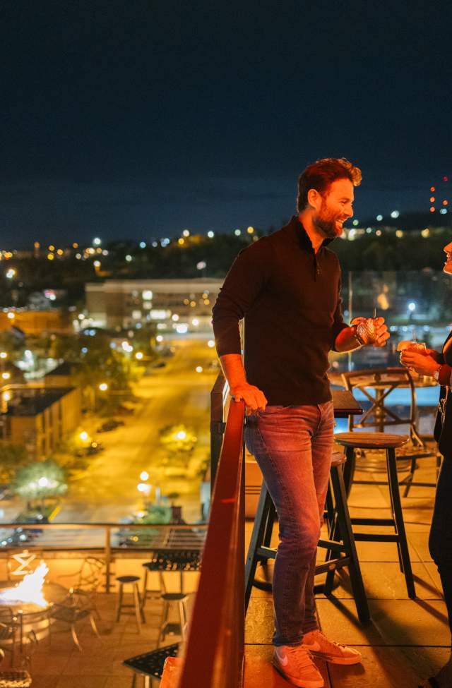 Couple clinking glasses in the evening surround by city lights on the roof of Vertex Sky Bar at Hotel Alex Johnson in Downtown Rapid City, SD