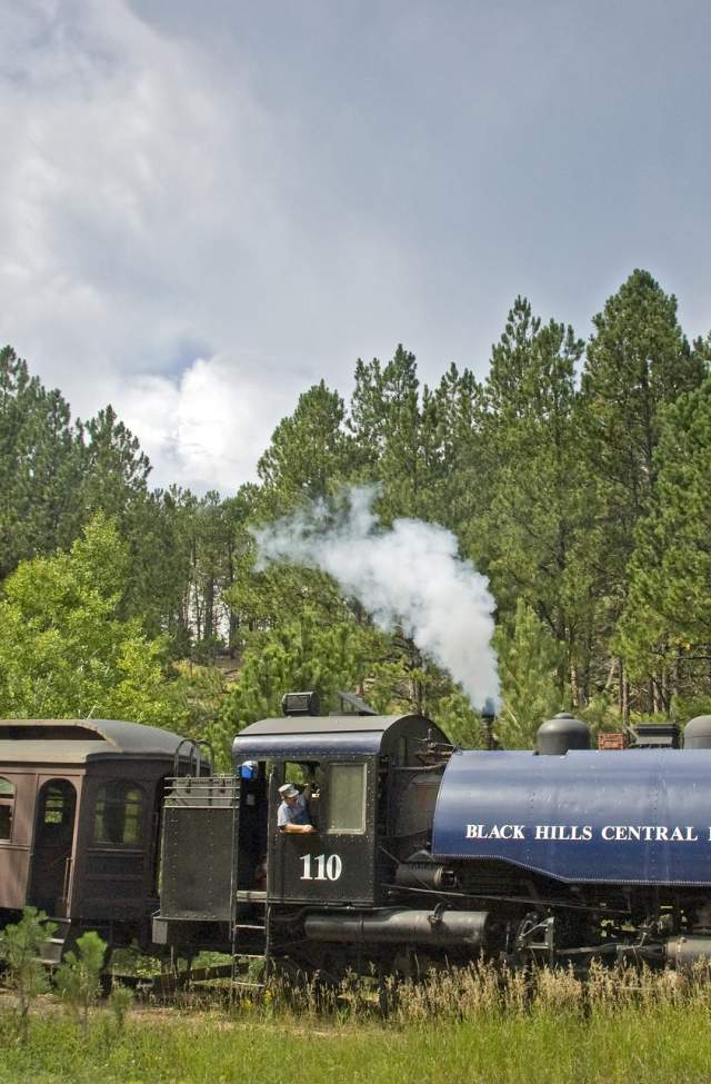 1880 train with passenger car making its way through the pine trees of the black hills in south dakota