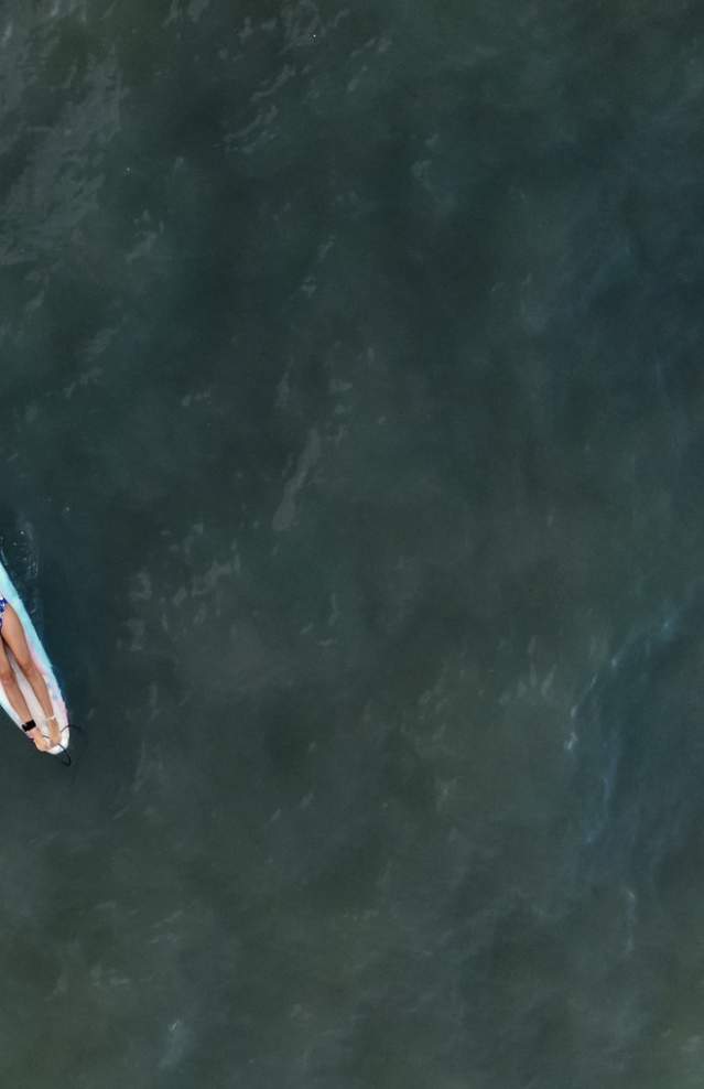 Drone shot of a woman relaxing on a surfboard in the ocean