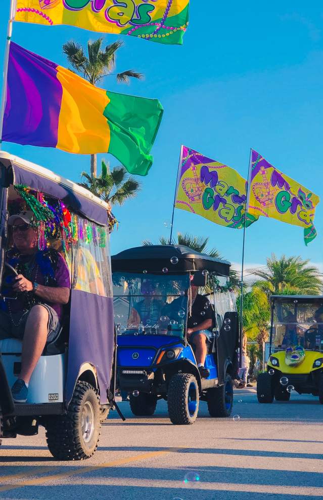 A golf cart parade goes by, each cart decorated with Mardi Gras colors and flags
