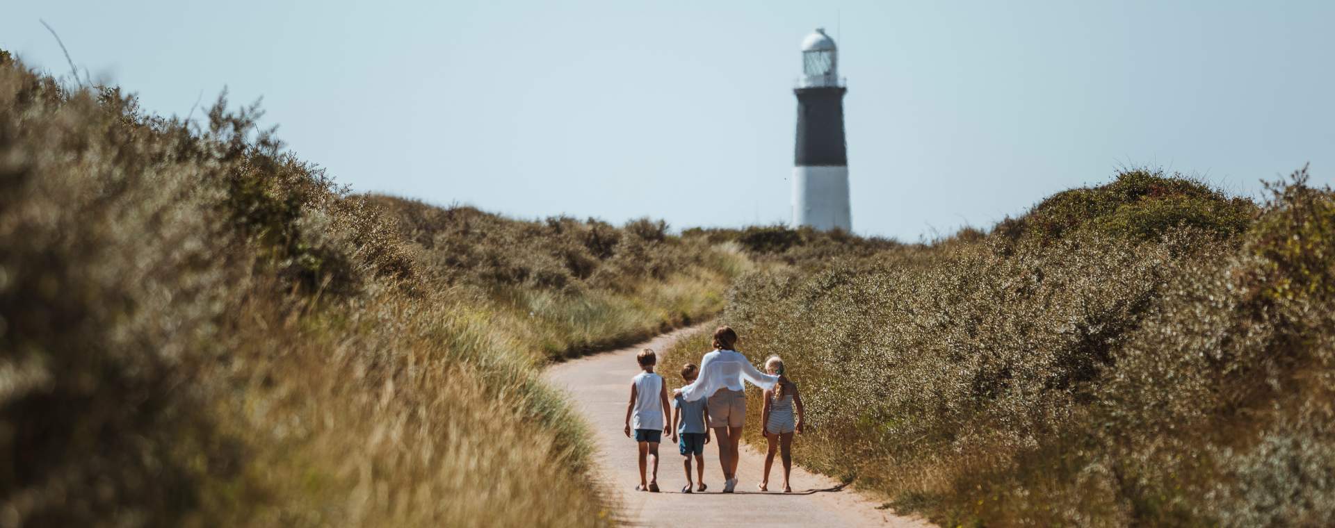 A family walking a winding path towards the iconic black and white Spurn Lighthouse in East Yorkshire