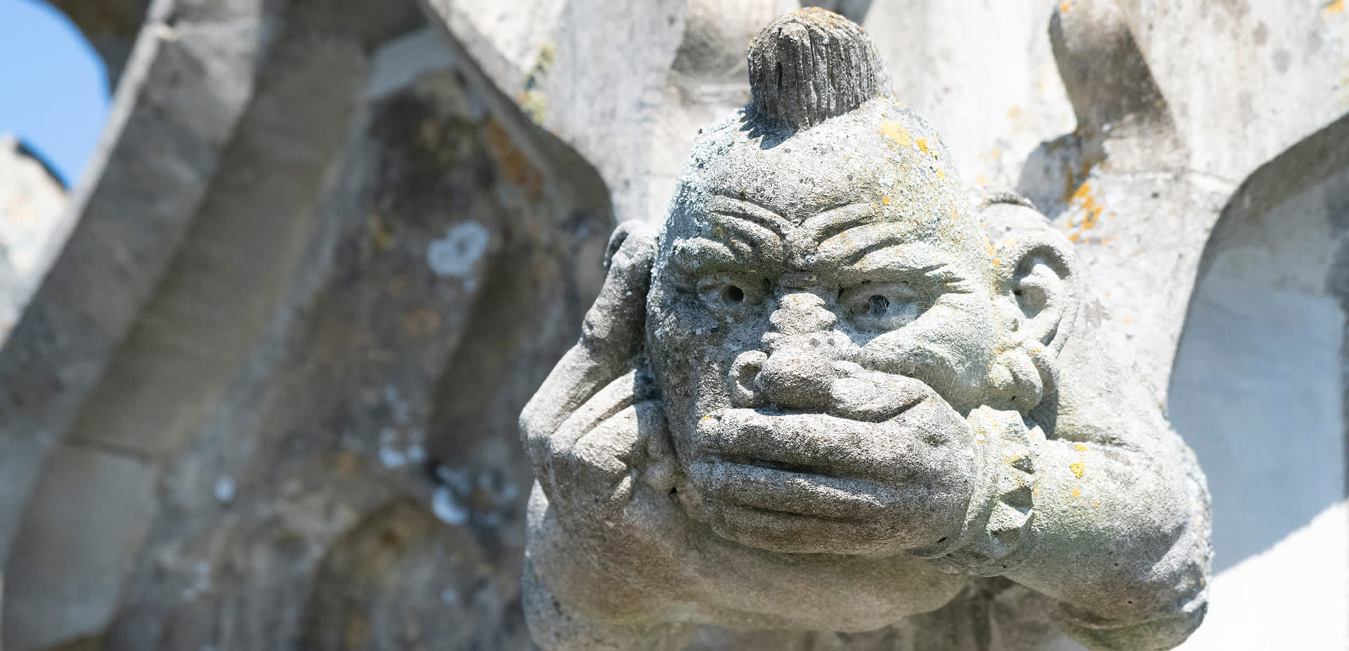A gargoyle with a mohican haircut and hand across his mouth on Cirencester church
