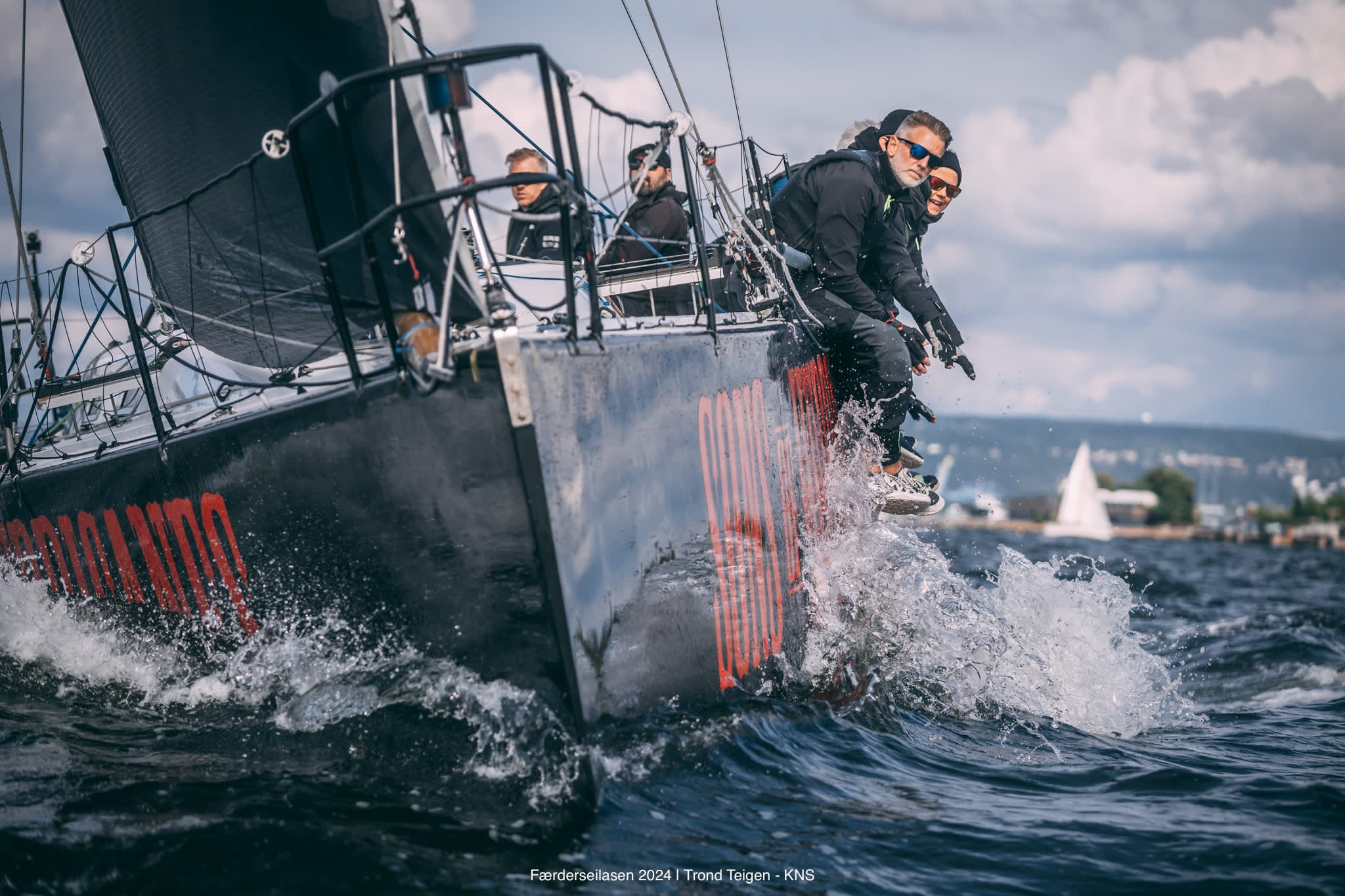 Menn som sitter på kanten av en seilbåt i full fart