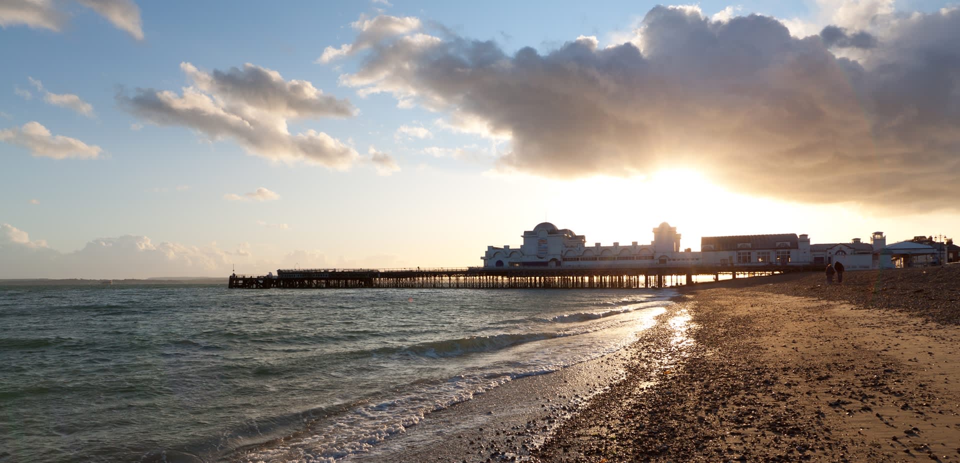 The sun sets behind South Parade Pier, with Southsea beach and sea in the foreground