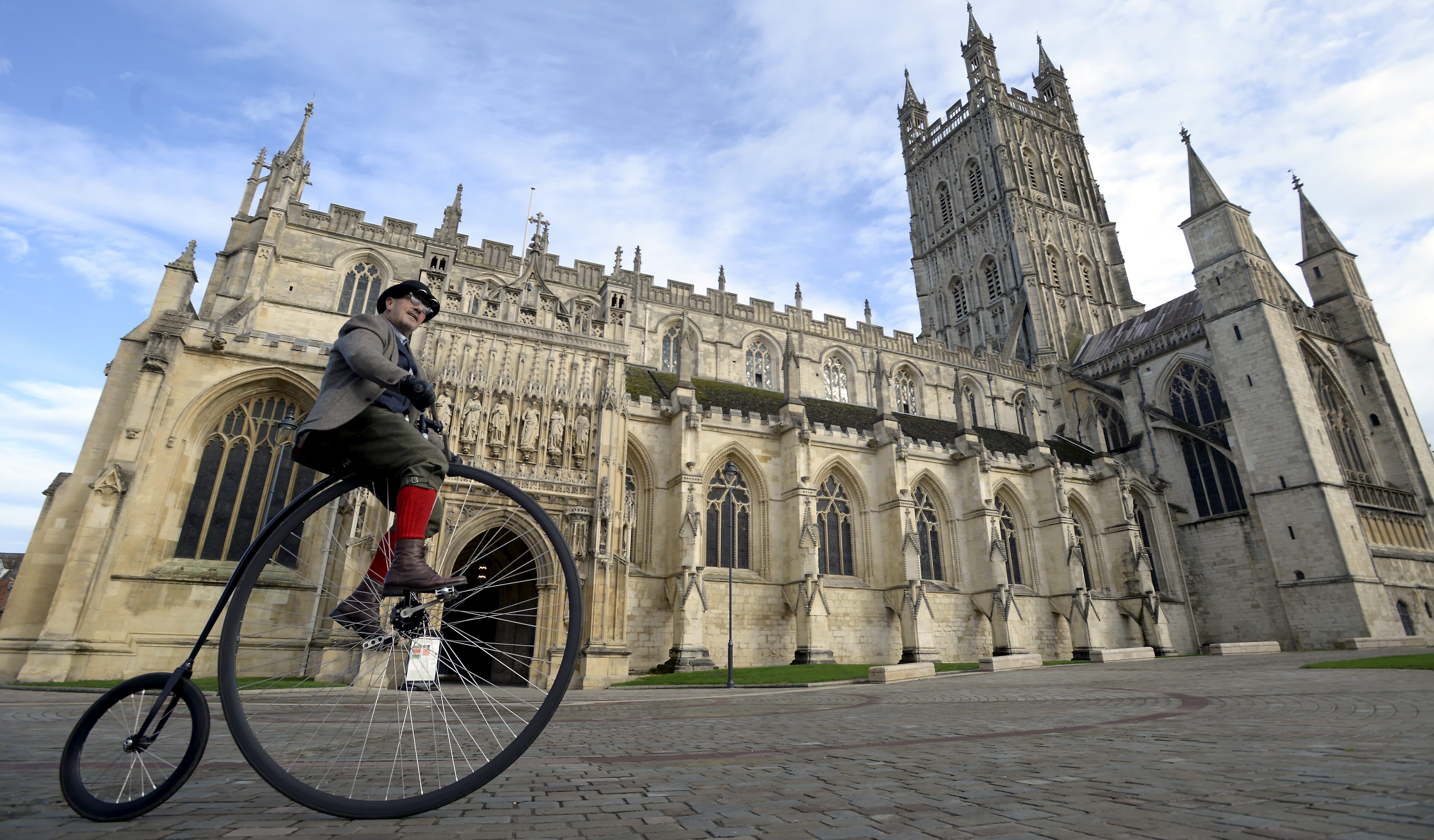 Man on a penny farthing bicycle in front of Gloucester Cathedral
