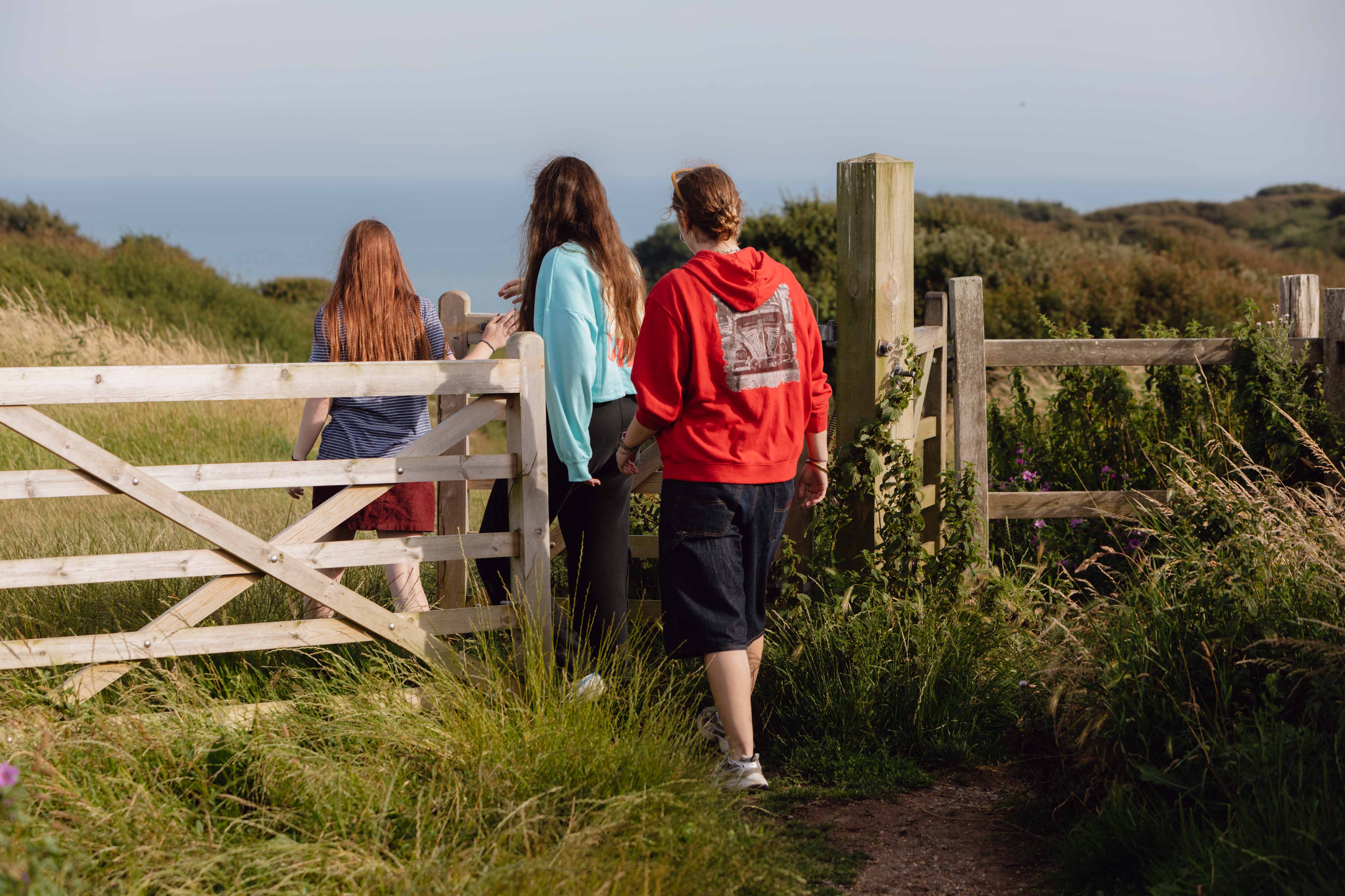 A group of 3 young people walking through a gate towards the sea on the Sussex Downs