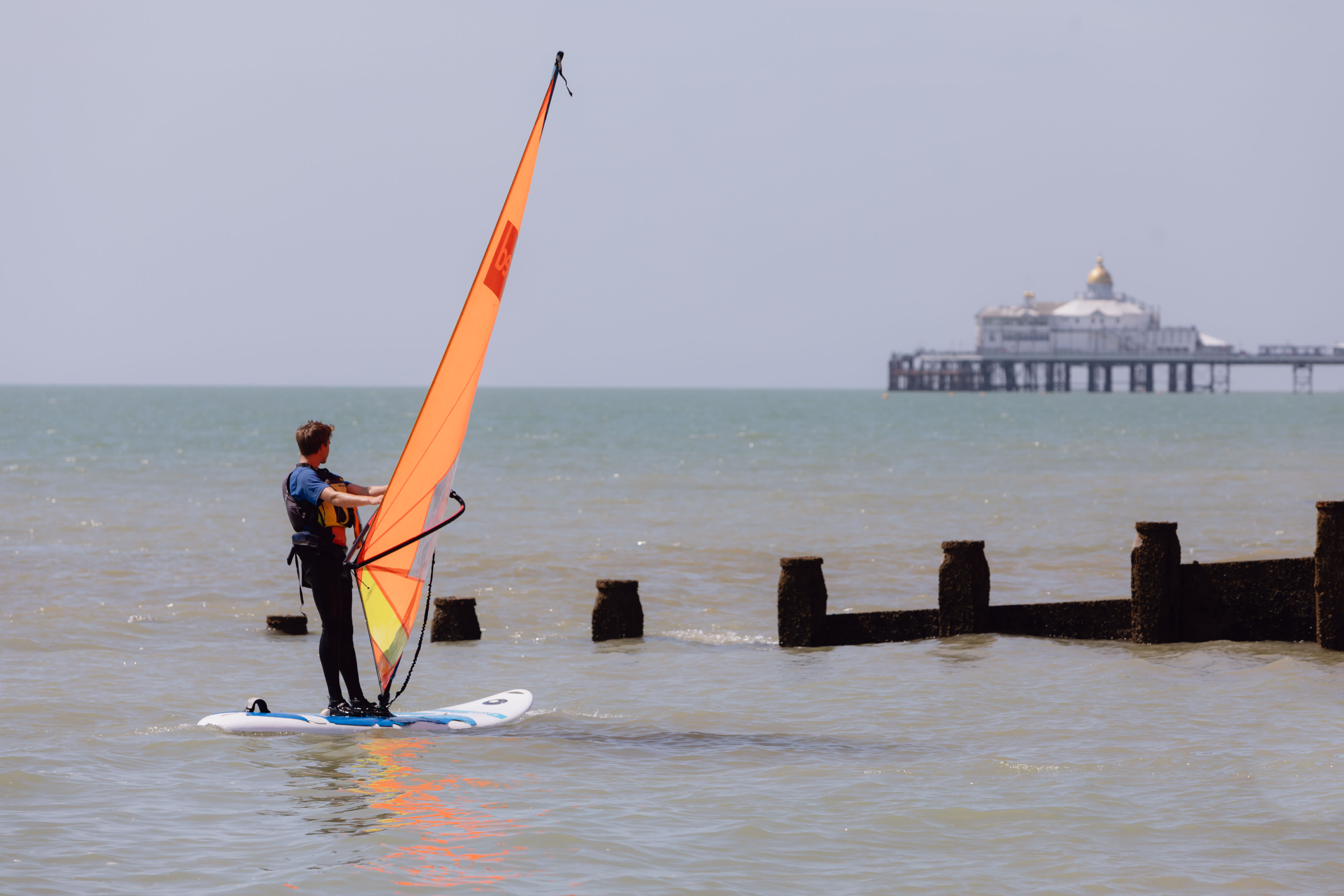 Windsurfer with orange sail looking at the pier on the Sussex coast