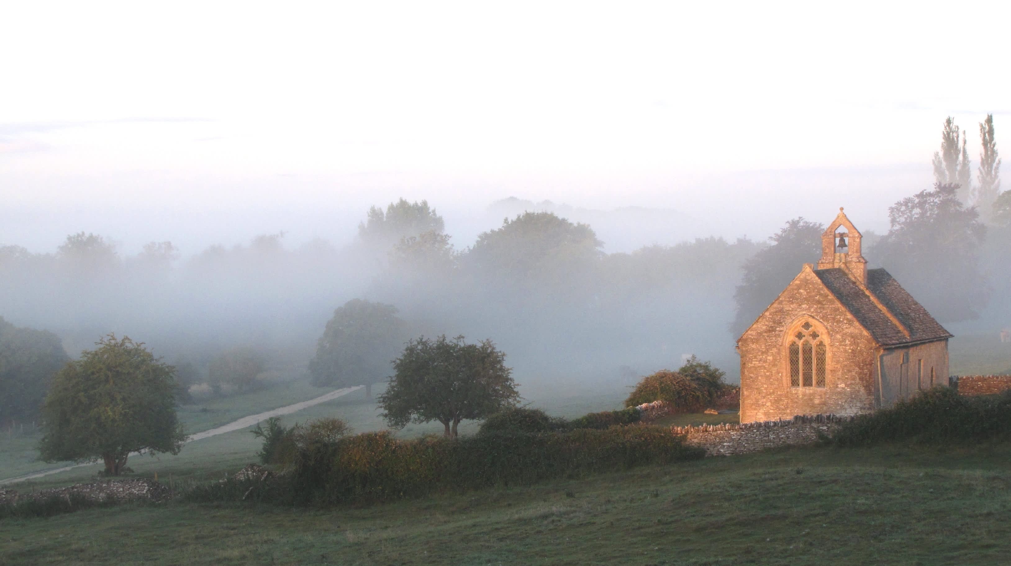 St Oswald's Church in Widford with sun on the building and an early morning mist (photo by Helena Sylvester)