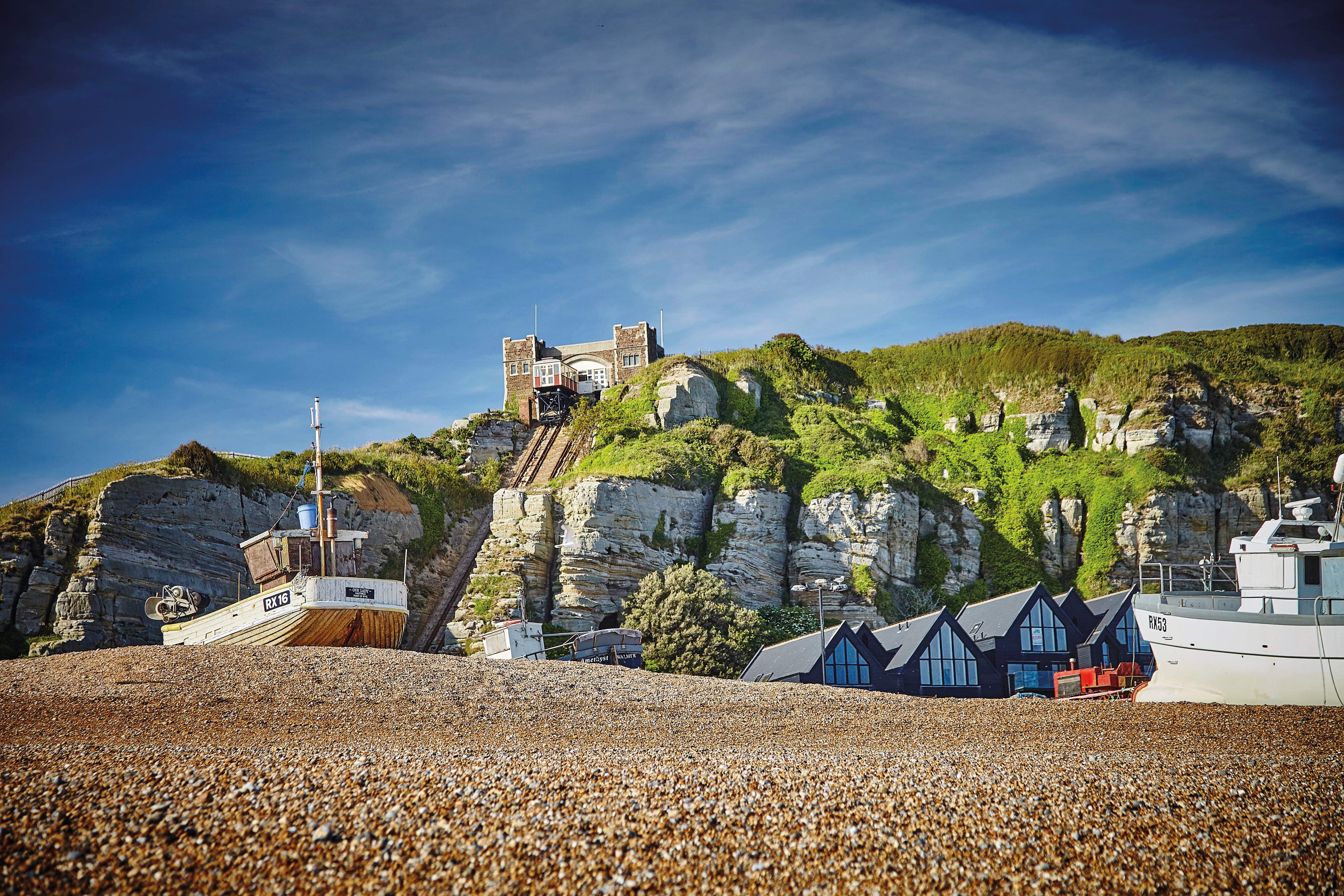 Shingle beach and fishing boat in Hastings Old Town, with cliffside lift in the background