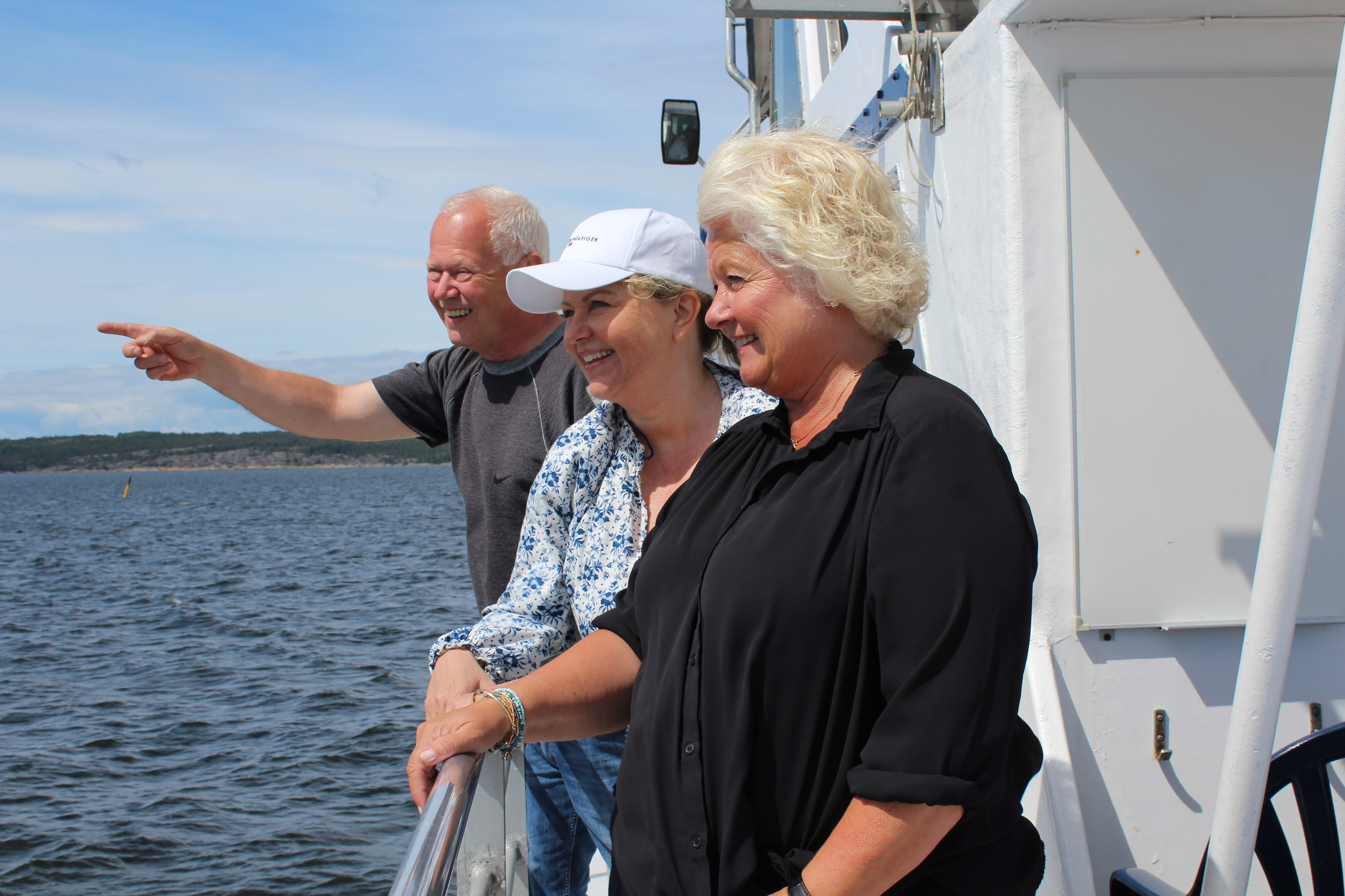 En mann og to kvinner står ved relingen på en båt og peker ut mot havet