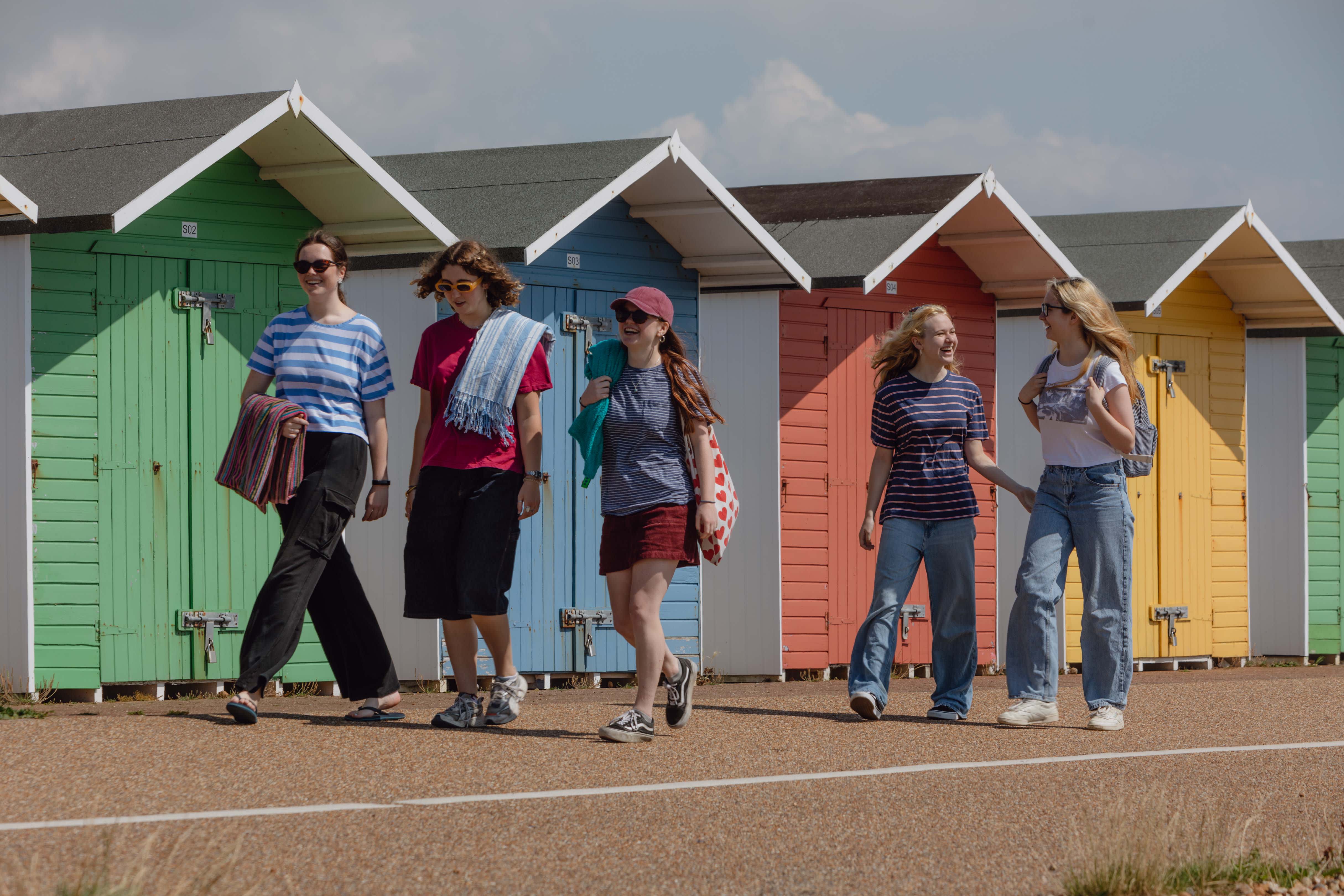 A group walking in front of multi colour beach huts in Sussex