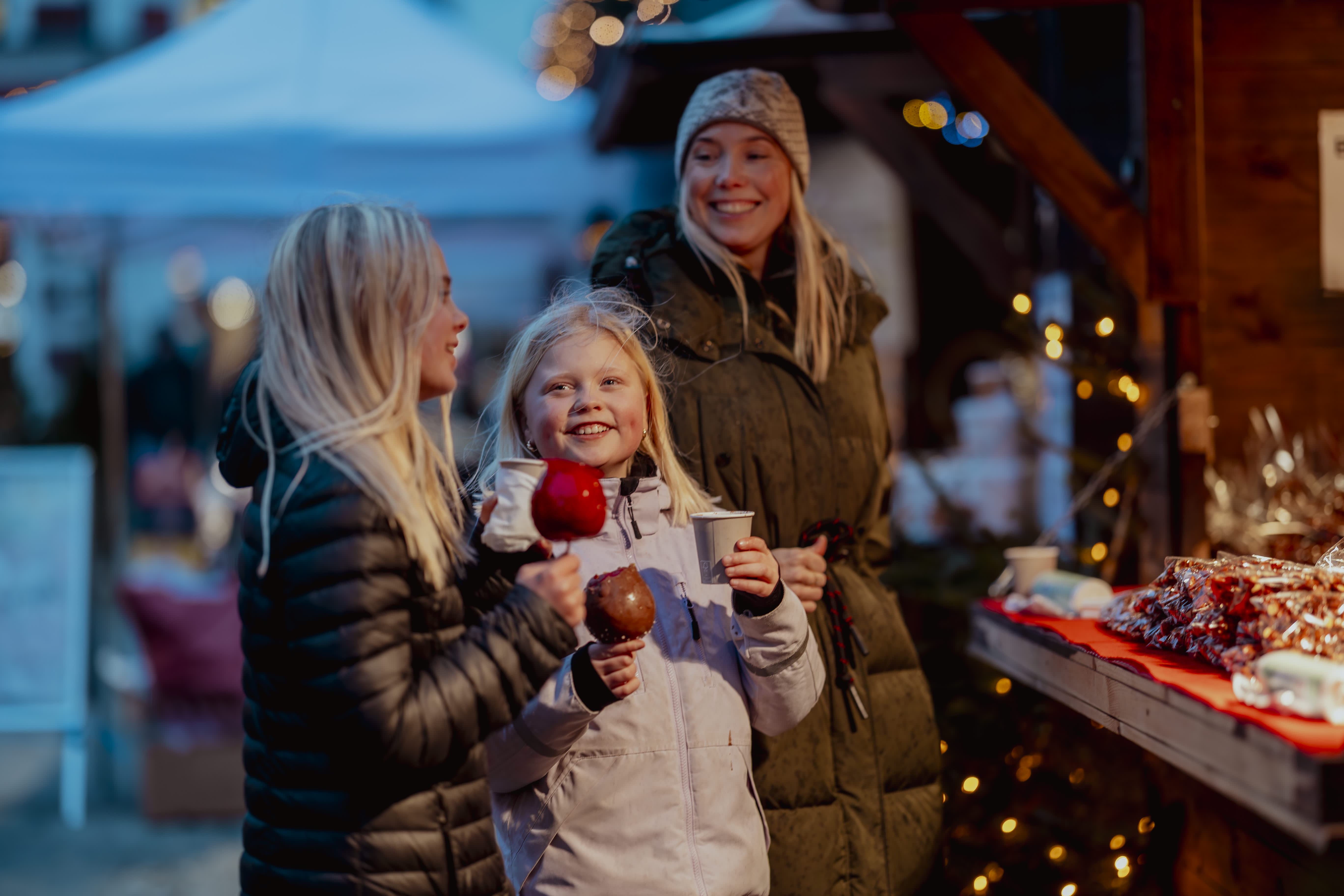 2 barn med godteri og 1 kvinne smiler ved julebodene i Kristiansand