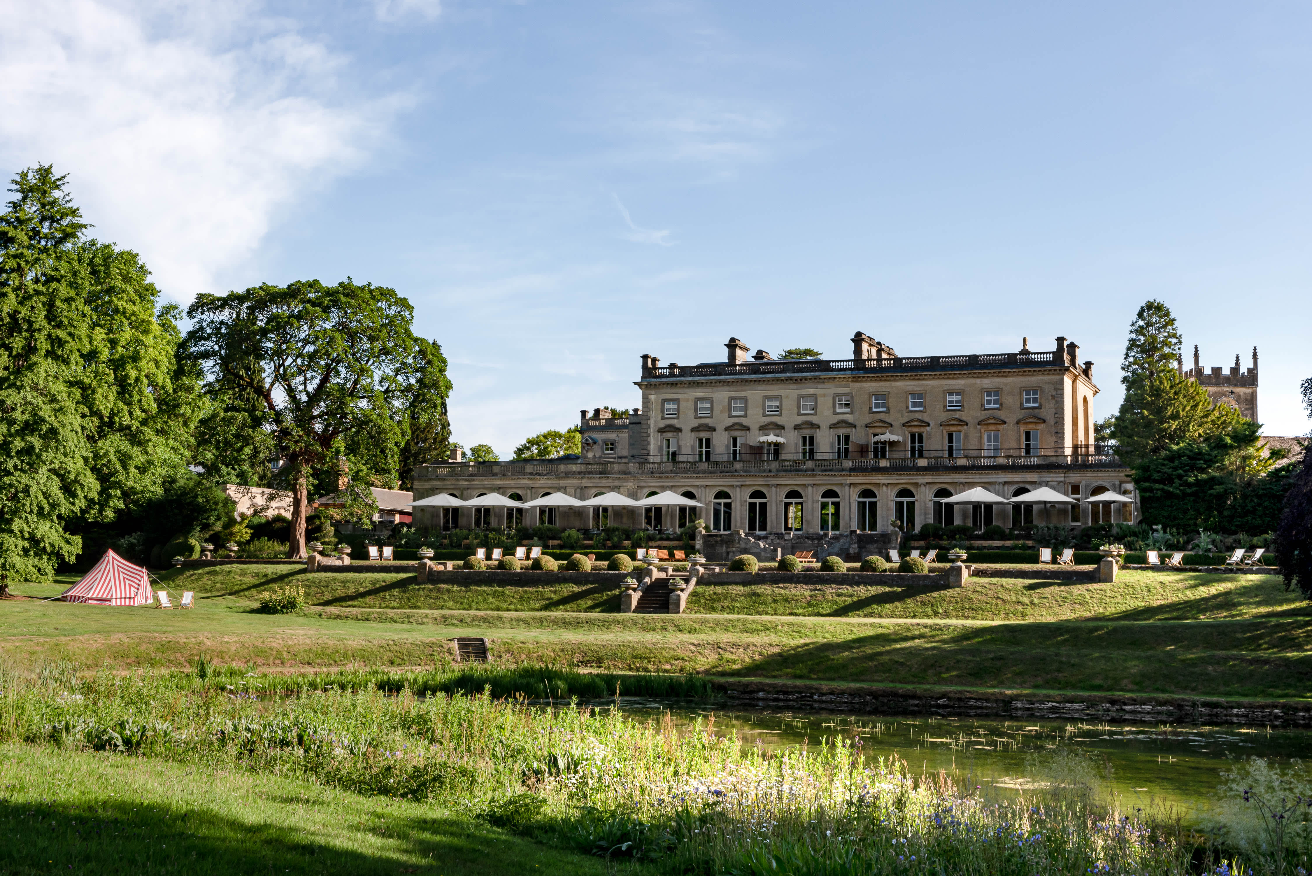 Stunning Cowley Manor surrounded by trees and a lake in its extensive grounds, in the Cotswolds