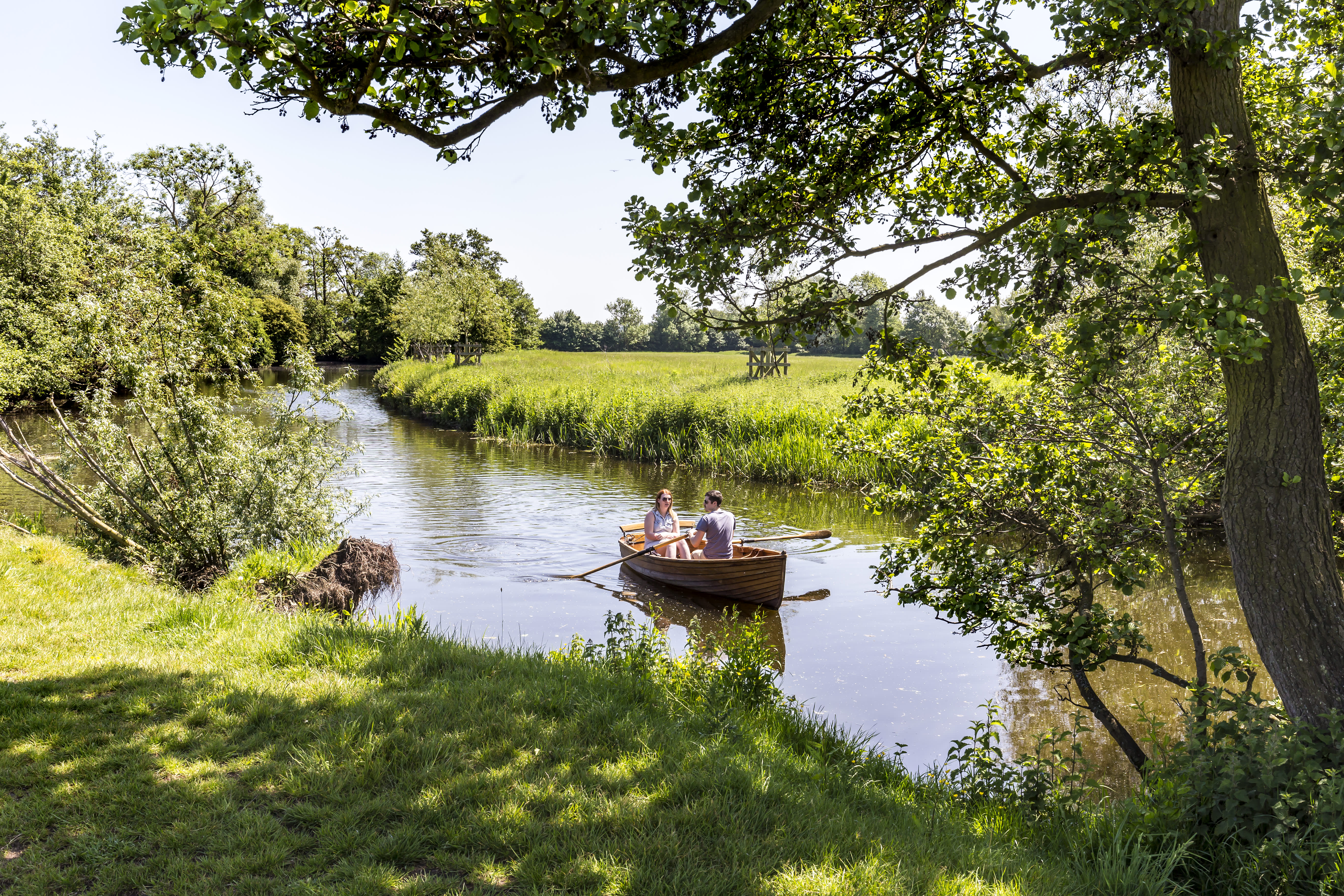 A couple are rowing a boat down a river in the picturesque countryside