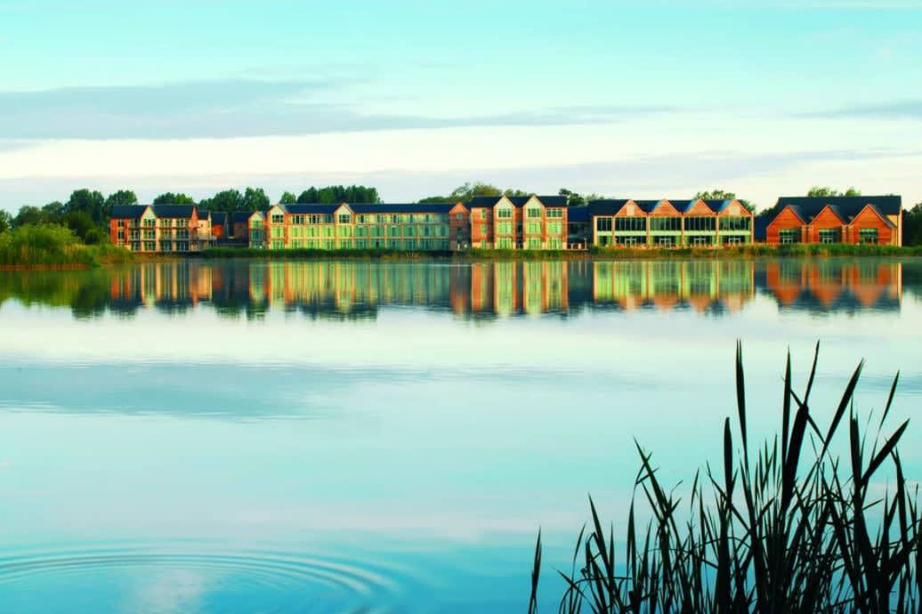 A Cotswold lake ripples in the breeze, in the distance the De Vere Cotswold Water Park stands on the lakeside