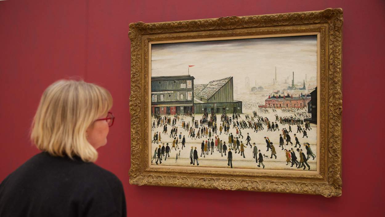 A person standing looking at the famous L S Lowry painting, Going To The Match.
