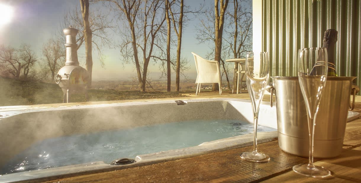 A bottle of champagne chills next to a hot tub with a breathtaking view of rolling hills at the Hilly Huts at the Fish Hotel in the Cotswolds