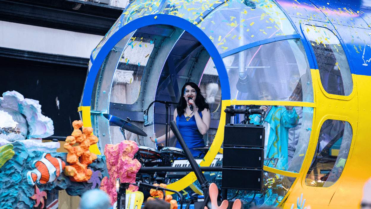 A lady dressed in a blue dress singing inside a large blue and yellow submarine