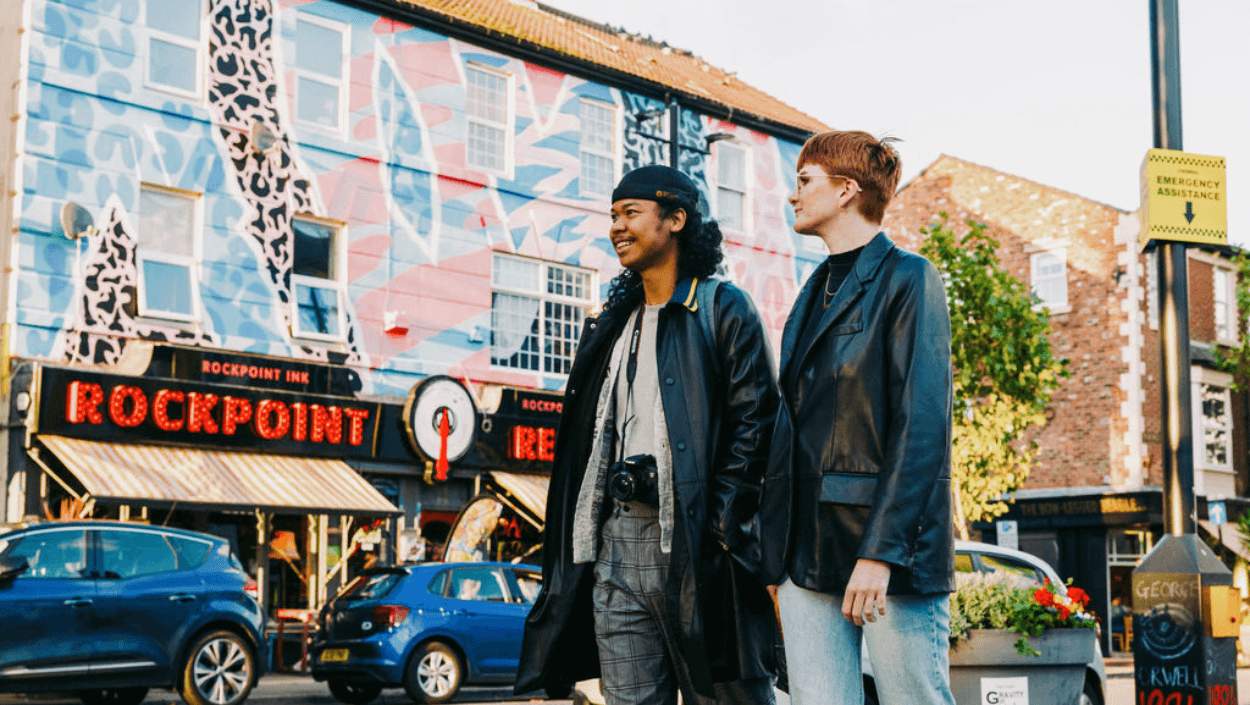 Two people stand on Victoria Road next to a venue called 'Rockpoint Records' that has pink and blue street art