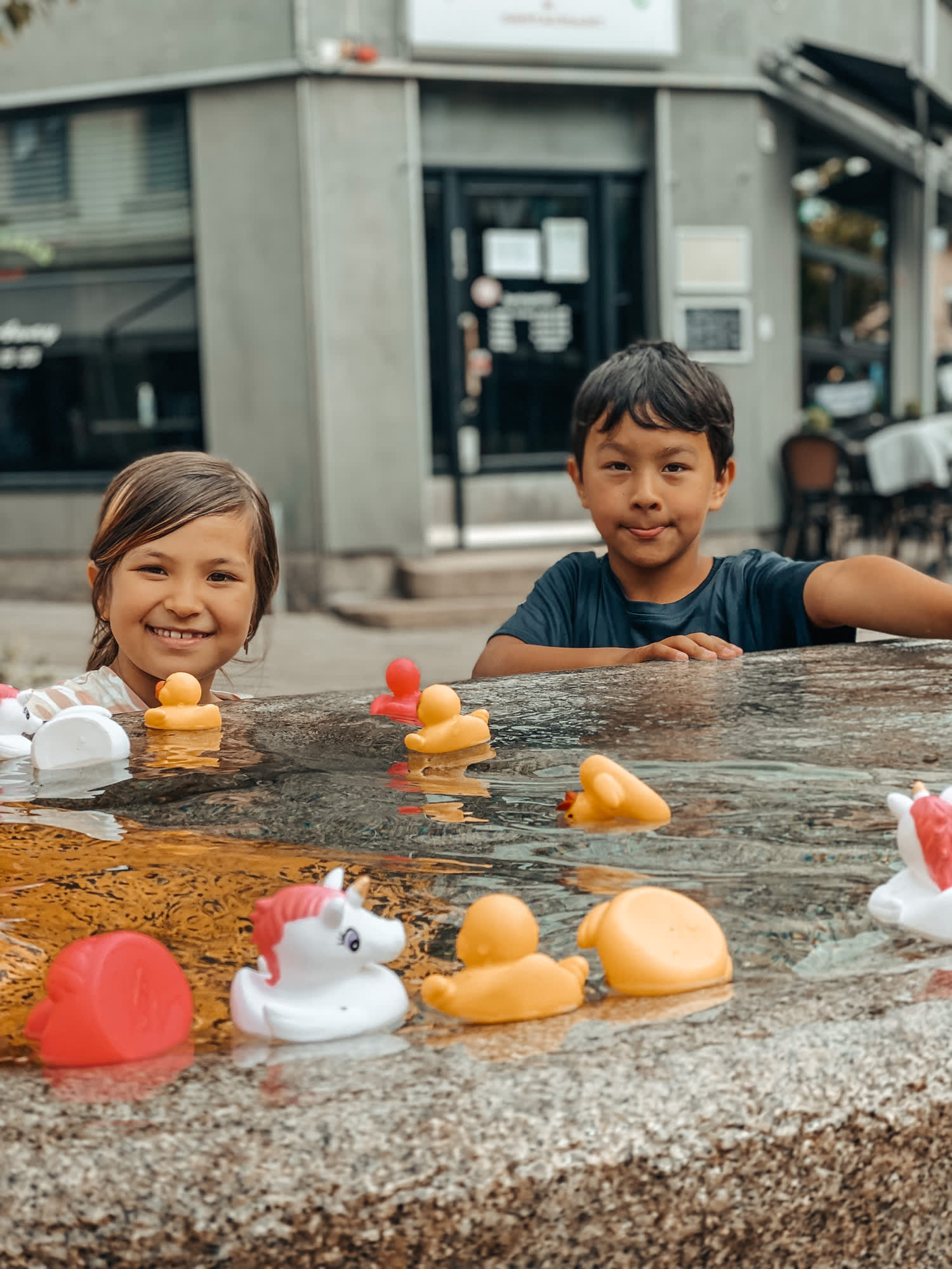 To små barn som leker med plastikk-badeender i vannskulpturen Flod. Foto.