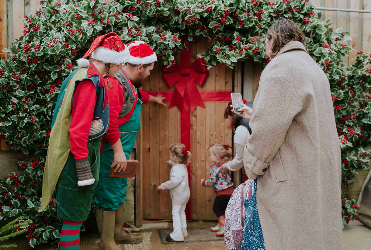 Two young children tentatively entering Santa's grotto with two 'elves'