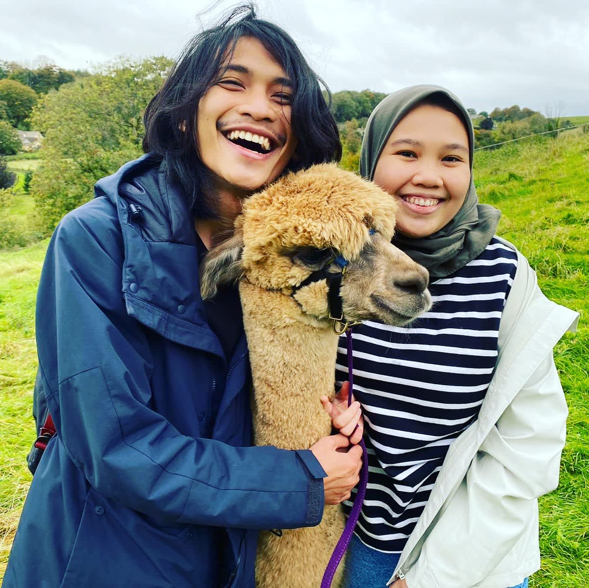 Two people smiling and posing with an alpaca