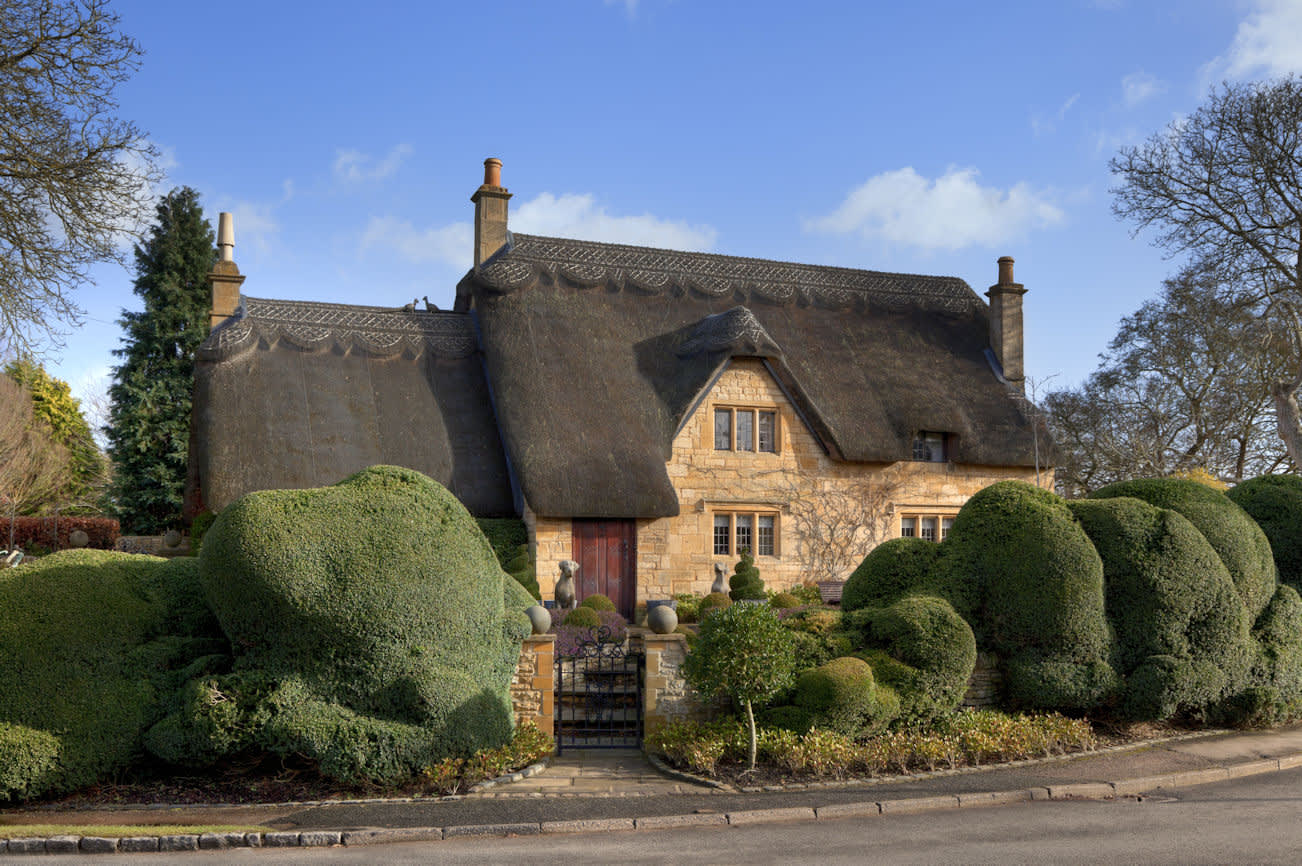 A beautiful thatched cottage surrounded by topiary trees from Manor Cottages in the Cotswolds