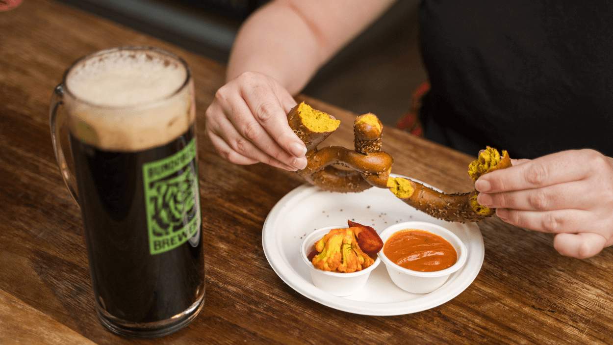 A table with a pretzel and a pint of beer.
