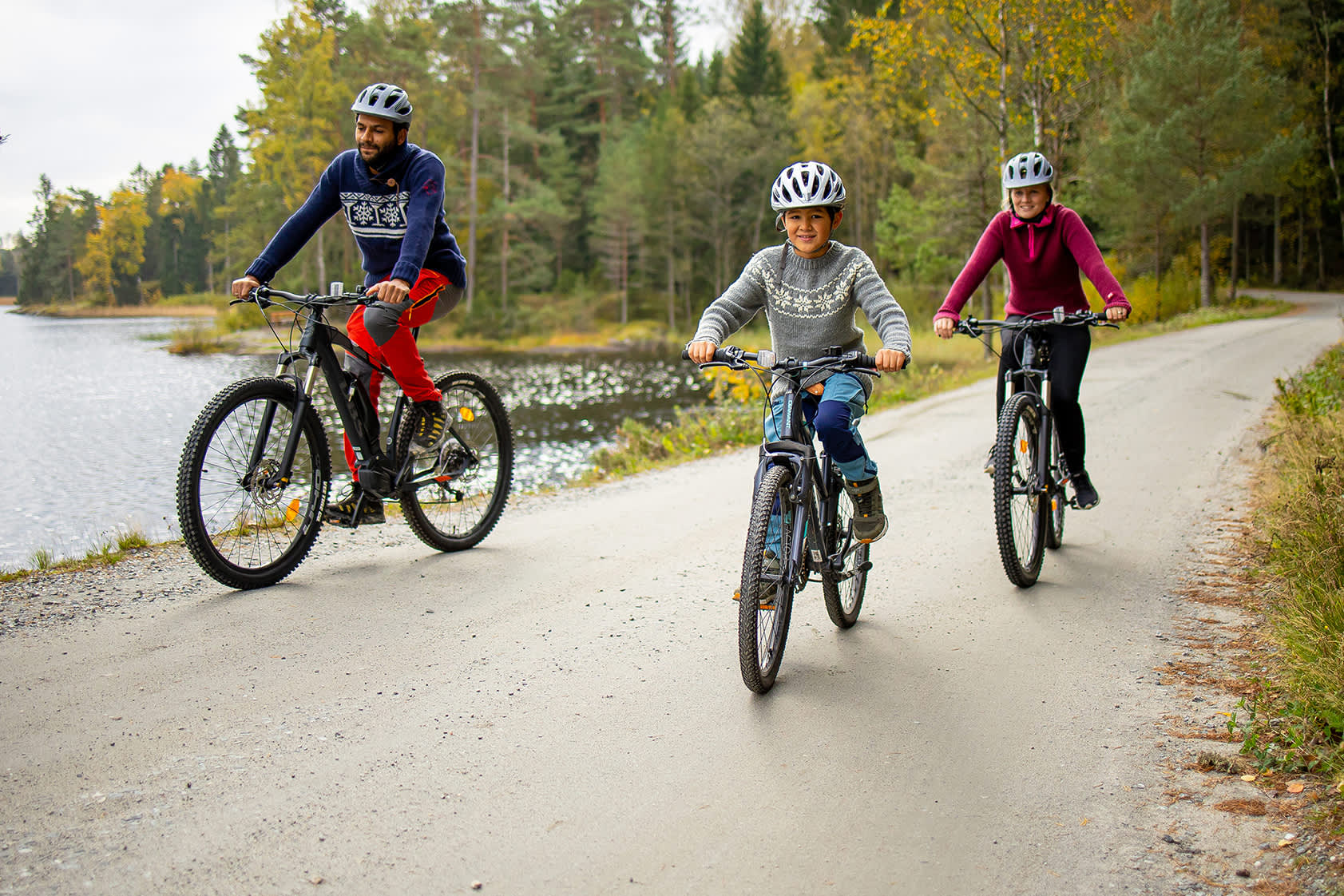Famile på sykkeltur på en grusvei langs et vann.