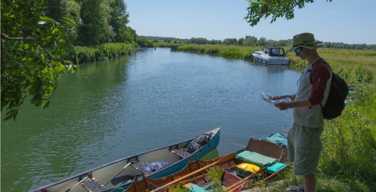 A man checks a map standing next to rowing boats moored on the River Thames, near Kelmscott