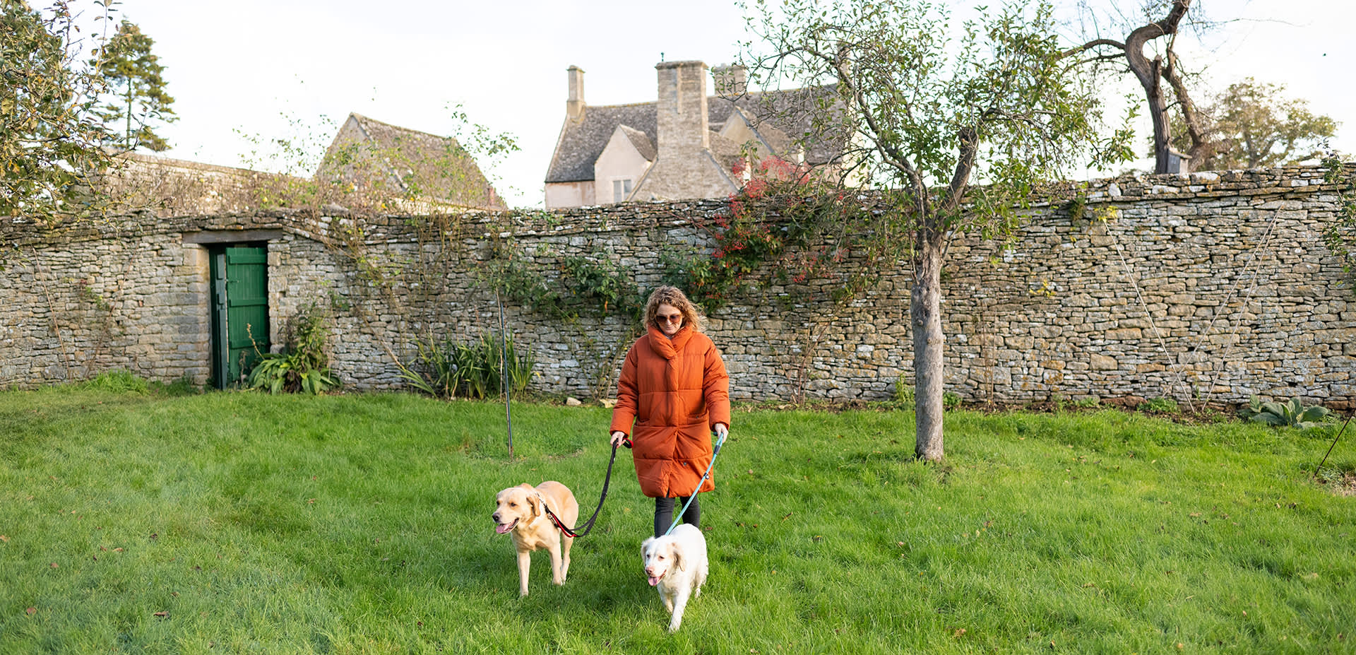 Woman with two dogs walking through the orchard at Cogges Manor Farm