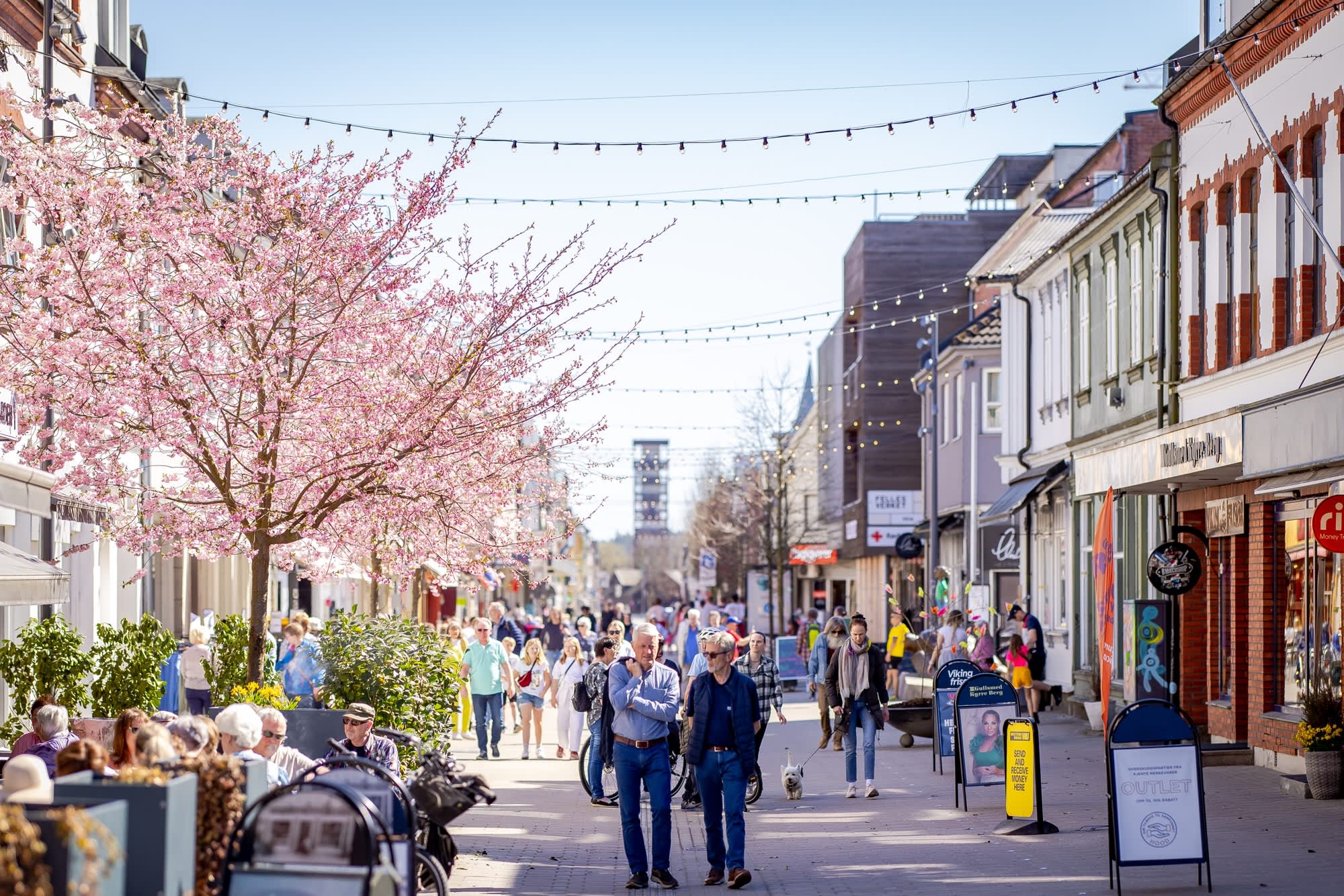 Mennesker som går i gågata og sitter på uteserveringen i Sarpsborg sentrum. Foto.