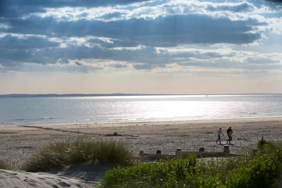 Sunny day at West Wittering beach looking out to sea, with a couple walking in the sandy dunes