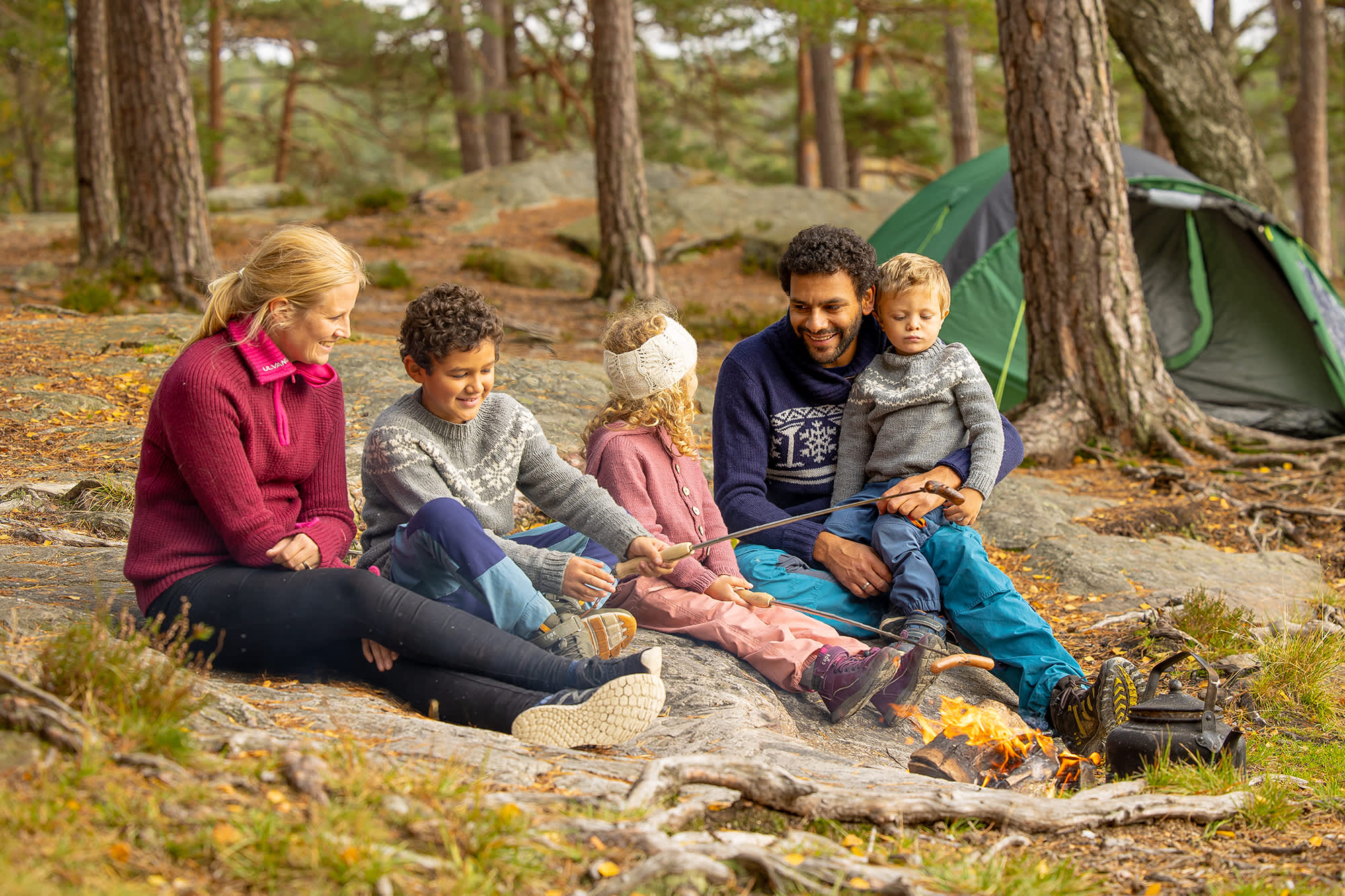 Familie på tur i skogen hvor de griller pølser.