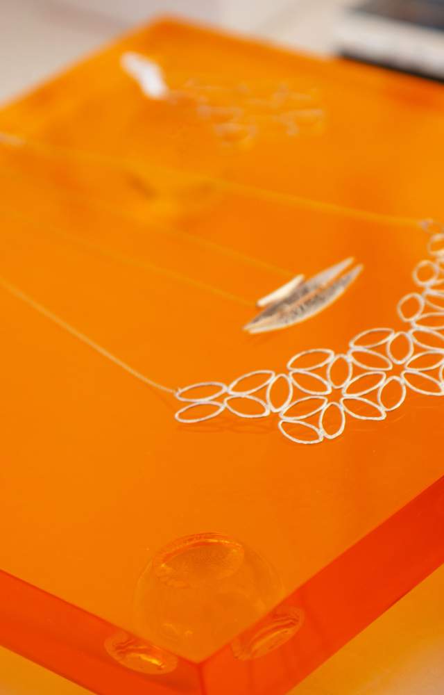 Handmade silver necklaces on display atop orange glass