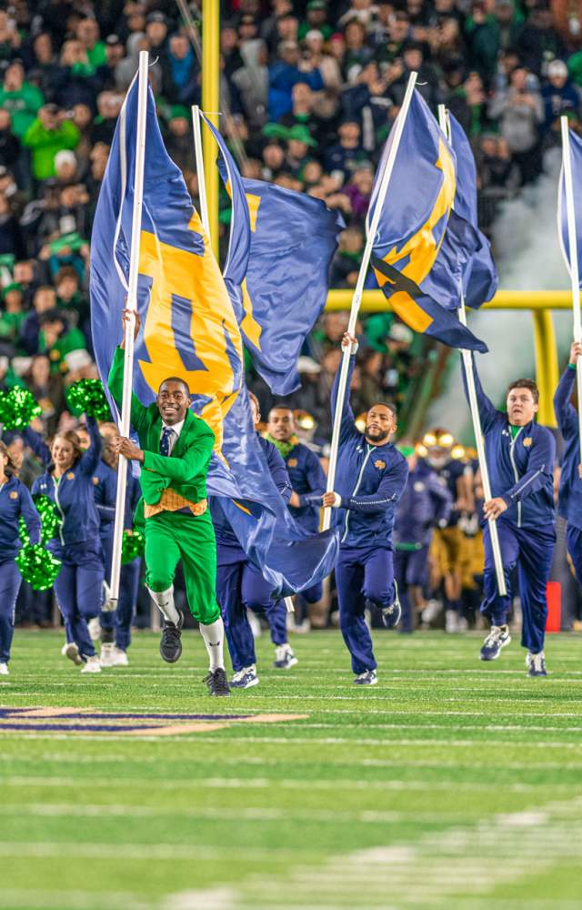 The Notre Dame Leprechaun and cheerleaders running down the field with flags