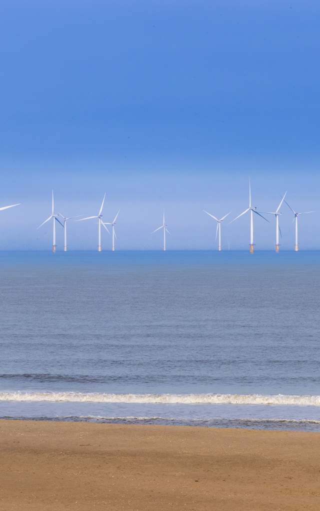 Offshore windfarms on the Lincolnshire Coast with a beach in the foreground under blue skies
